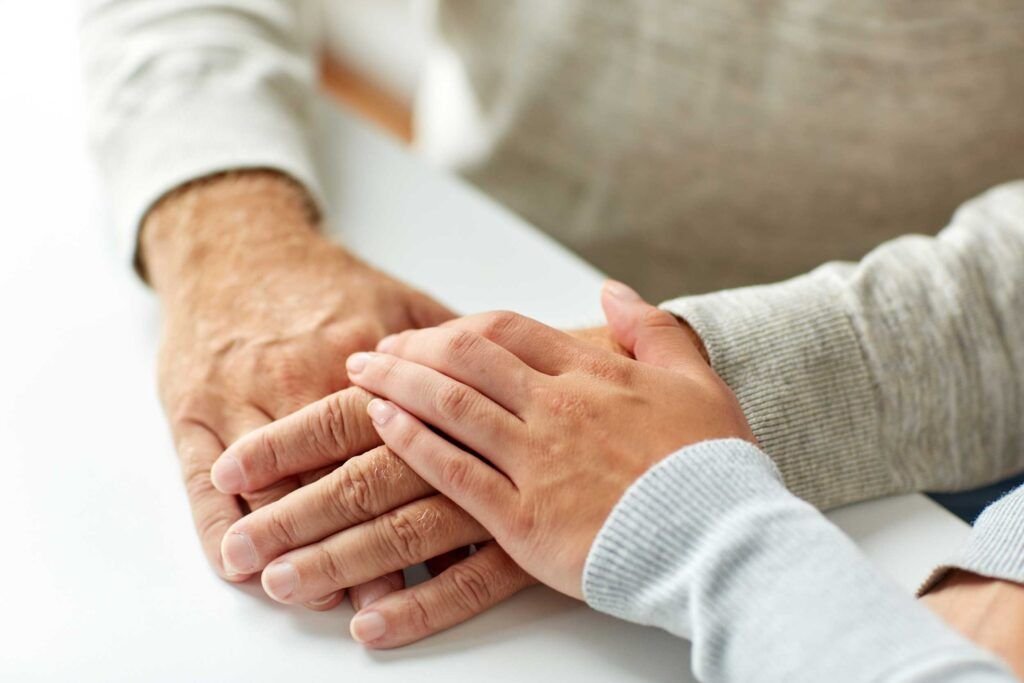 Betreuungskraft legt ihre Hand auf die Hand eines älteren Mannes